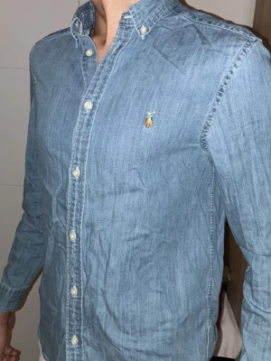 Blå skjorta från Ralph Lauren - Klassisk blå skjorta från Ralph Lauren med broderad logga på bröstet. Skjortan har knappar framtill och på kragen samt lång ärm. Perfekt för en stilren och avslappnad look. Den är gjord för en perfekt Frankrike strand ute på stranden. Samt att den passar perfekt med vanliga basic jeans 👖. När du har på dig denna skjortan så känner du dig nästa som Mick Ross första dagen på jobbet och du inte har någon aning vad du ska ha på dig. Skriv om ni är intresserade 👏💫😗