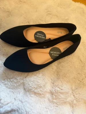 Svarta ballerinaskor - Helt nya aldrig använda svarta ballerinaskor med spetsig tå och mjuk innersula i memory foam för extra komfort. Storlek 42 men passar även strl 41 som jag har. Skorna har en enkel och klassisk design som passar till många olika outfits. Materialet ser ut att vara textil med en matt finish. 