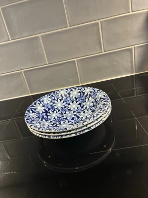 3 stycken Blåvita blommiga tallrikar i keramik - Tre stycken runda tallrikar i keramik med blå botten och vitt blommönster. Perfekta för att piffa upp köket eller servera mat på ett snyggt sätt. Tallrikarna har en klassisk form och ett detaljerat mönster som sticker ut.