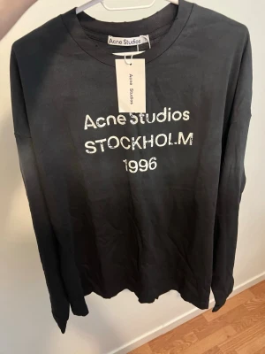 Svart långärmad t-shirt Acne Studios - Svart långärmad t-shirt från Acne Studios med tryck 'Acne Studios STOCKHOLM 1996' i vitt framtill. Klassisk rund halsringning och relaxed passform. Tillverkad i mjuk bomull för en bekväm känsla. Perfekt för en stilren och enkel look.