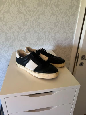 Valentina flycrews läder - Snygga svarta flycrews med vit panel på sidorna och vit sula. Skorna har klassisk låg profil och svarta skosnören. Tillverkade i läder med en stilren och tidlös design som passar till det mesta. Lite slitna men fortfarande mycket kvar att ge, valentino dustbag medföljer. Saknas 3 nitar 