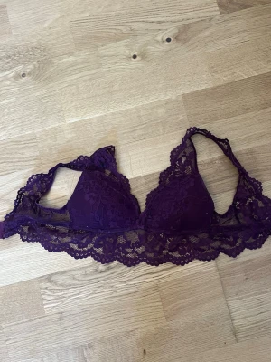 Lila spetsbralette med vaddering - Snygg lila bralette med vadderade kupor och bred spetskant. Modellen har tunna axelband och är tillverkad i mjuk spets med blommönster. Perfekt för dig som gillar en feminin och bekväm stil.