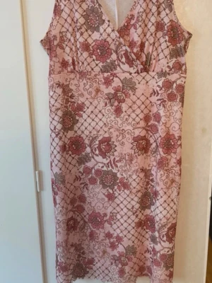 Blommig rosa klänning Bon'A Parte - Söt ärmlös klänning från Bon'A Parte i ljusrosa med blommigt mönster i rött och grönt. Klänningen har omlott-ringning och knälång passform. Perfekt för dig som gillar romantiska och feminina plagg🩷