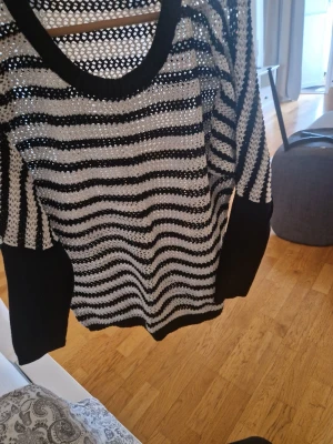 Randig stickad tröja från KappAhl - Säljer en svartvit stickad tröja från KappAhl med breda ränder och hålmönster. Tröjan har rund halsringning, långa ärmar och ribbade muddar. Perfekt för lager på lager och ger en cool, avslappnad look.