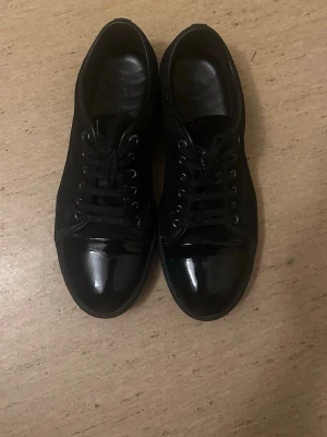 Svarta sneakers med lackdetaljer - Lanvin Dust bag följer med. Snygga helsvarta sneakers med glansiga lackdetaljer på tån och klassisk snörning. Skorna har en låg profil och stilren design som passar till det mesta. Materialet är en mix av textil och lack, vilket ger en cool kontrast. Dom är lite smutsiga men de går att tvätta bort:) pris går att diskutera 