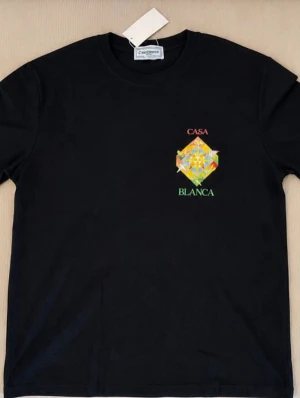 Svart  t-shirt med tryck  - Svart t-shirt från casablan med färgglatt grafiskt tryck och texten 'CASA BLAN på både bröstet och ryggen. Klassisk passform och rund hals. Tillverkad i mjuk bomull som känns skön mot huden. Perfekt för dig som gillar streetwear och unika prints.