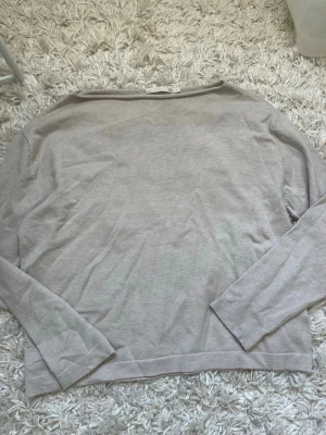 Ljusgrå tröja från 157 - Ljusgrå långärmad tröja från 157 med enkel och stilren design. Tröjan har rund halsringning och är tillverkad i ett mjukt material som passar perfekt för en avslappnad look. Perfekt att matcha med jeans eller leggings.