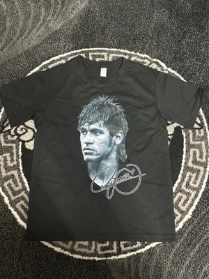 Svart t-shirt med tryck och text - Cool svart t-shirt med stort tryck av ett ansikte och signatur på framsidan samt sköld och texten 'The prince who never became a king' på baksidan. Klassisk passform och rund hals. Perfekt för dig som gillar statement-plagg.