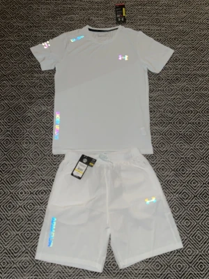 Vitt träningsset från Under Armour - Snyggt vitt träningsset från Under Armour med t-shirt och shorts. Setet har holografiska loggor och detaljer, samt UA Sports- och Under Armour-tryck. Tillverkat i ett lätt och snabbtorkande funktionsmaterial som passar perfekt till träning.