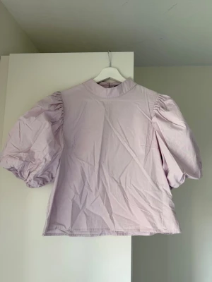 Ljuslila blus med puffärm Gina Tricot - Trendig ljuslila blus från Gina Tricot med högt halsringning och stora puffärmar. Perfekt för att lyfta vilken outfit som helst.