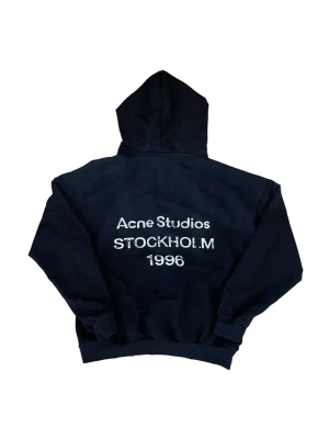 Svart hoodie Acne Studios Stockholm - Svart hoodie från Acne Studios med stor huva och tryck på ryggen där det står 'Acne Studios STOCKHOLM 1996'. Klassisk passform med ribbade muddar vid ärmslut och nederkant. Perfekt för en avslappnad och cool stil.