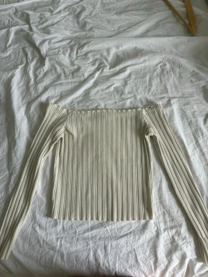 Offshoulder ribbad topp i vitt - Trendig offshoulder topp i ribbad vit bomullsmix. Långärmad och tight passform som sitter snyggt på kroppen. Perfekt att styla med jeans eller kjol för en clean och modern look.