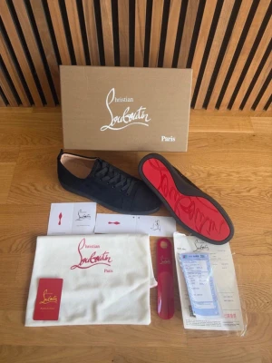 Svarta Christian Louboutin sneakers - Snygga svarta sneakers från Christian Louboutin med klassisk röd sula och diskret logga. Skorna har en låg profil, rund tå och är tillverkade i slätt läder. Perfekta för dig som vill ha en exklusiv och stilren look. Storlek 43 vid frågor eller funderingar är de bara att höra av sig!