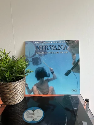Nirvana Greatest Hits On Air (Blue) (Vinyl) LP - Rare Limited edition LP med Nirvana Greatest Hits Live On Air, pressad på blå vinyl. Omslaget har ikoniskt undervattensmotiv och innehåller låtar som Smells Like Teen Spirit, Come As You Are och In Bloom. Perfekt för samlare och fans av klassisk grunge. Skivan är rund och gjord av vinyl.