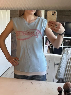 2000s topp  - Säljer en ljusblå ärmlös topp från vintage hm med ett rosa tryck. Köpt secondhand, använd 1 gång på spex💓 storlek L men sitter som S 