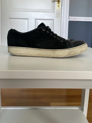 Svarta lanvins låda dust bag saknas  - Snygga svarta sneakers med ovandel i mocka och detaljer i läder. Skorna har vita sulor med en något sliten look och klassisk snörning med metallhål. Perfekta för en clean och stilren outfit.