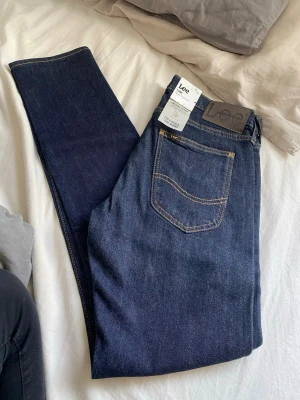 Mörkblå slim tapered jeans från Lee - Snygga mörkblå jeans från Lee i modellen Luke med slim tapered passform. Klassisk femficksdesign, kontrastsömmar och Lee-läderpatch bak i midjan. Tillverkade i slitstarkt denimtyg som ger en clean och modern look. Helt nya med lappar kvar, pruta om så vill☺️
