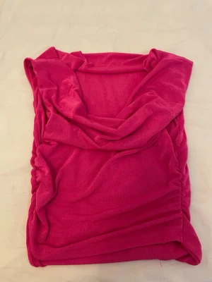 Rosa omlott linnetopp - Snygg rosa linnetopp med omlott-detalj och djup v-ringning. Toppen är ärmlös och har en draperad look som ger en cool och trendig vibe. Perfekt att styla med jeans eller kjol för en färgstark outfit.