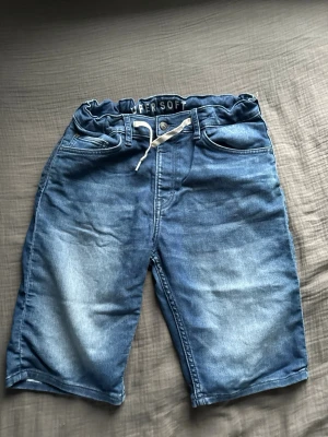 Blå jeansshorts med snörning - Säljer ett par blå jeansshorts från Super Soft med snörning i midjan och klassisk femficksdesign. Shortsen har en avslappnad passform och är tillverkade i mjuk bomull med elastisk midja för extra komfort. Perfekta för sommardagar!
