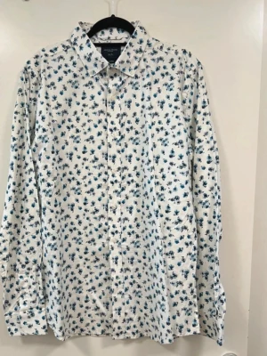 Vit blommig skjorta från Grand Frank - Snygg vit skjorta från Grand Frank med blått blommigt mönster. Skjortan har klassisk krage, knäppning framtill och långa ärmar. Perfekt för dig som vill sticka ut lite extra med en fräsch och modern look.