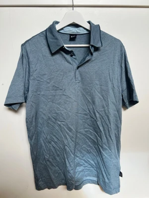 Blå pikétröja från Hugo Boss - Klassisk blå pikétröja från  Hugo  Boss med krage och knappar framtill. Tröjan har korta ärmar och är tillverkad i ett mjukt bomullsmaterial. Perfekt för en avslappnad men stilren look.
