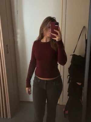 Mörkröd långärmad topp - En enkel och stilren mörkröd långärmad topp med rund hals. Modellen är tight och croppad vilket ger en modern look. Perfekt att matcha med både jeans och kjol för en trendig outfit.