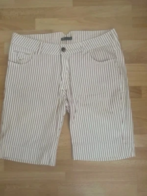 Randiga vita shorts med fickor - Snygga vita shorts med tunna vertikala ränder i rött och blått. Klassisk femficksmodell med knapp och dragkedja framtill samt två bakfickor med knapp. Perfekta för sommaren och har en avslappnad passform. Använd en gång, midjan 88cm.