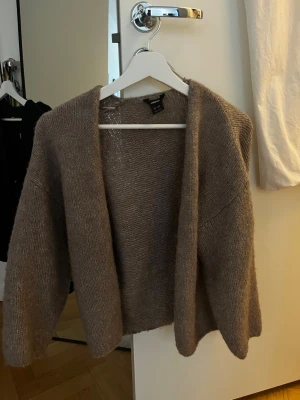 Beige stickad kofta från Lindex - Mysig beige stickad kofta från Lindex med öppen front och avslappnad passform. Koftan har långa ärmar och är tillverkad i ett mjukt, fluffigt material som passar perfekt för lager på lager. Enkel och stilren design som är lätt att matcha.