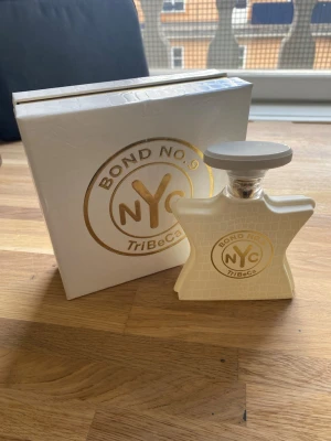Bond No. 9 TriBeCa parfym NYC - Exklusiv parfym från Bond No. 9 i modellen TriBeCa. Flaskan är vit med krokodilstruktur och har gulddetaljer samt ett stort runt lock. Kommer i en matchande vit och guld presentförpackning med NYC-logga. Perfekt för dig som gillar lyxiga dofter och snygg design. Flaskan har endast använts ett fåtal gånger 90% av innehållet är kvar.