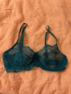 Turkos spets-bh från Hunkemöller - Hunkemöller bh i modellen ”Isabel” i storlek 70D. Bh:n är tillverkad i genomskinlig spets med justerbara axelband och bygel för extra stöd. 