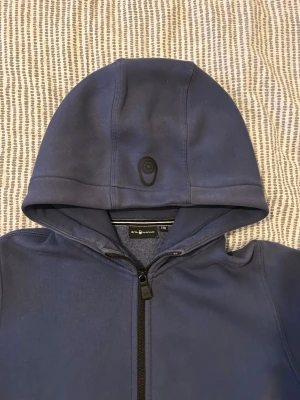 Sail Racing - Mörkblå ziphoodie från Sail Racing. Hoodien är i bra skick, men märket som satt på sidan har åkt av. Därför syns ett lim-märke. Men ingen man tänker på när armarna ligger över. Köpte för runt 800. Jag är 174 och den sitter bra på mig.