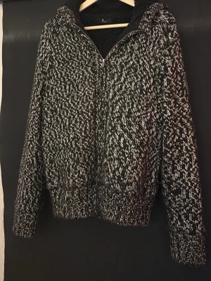 Svartvit stickad ziptröja Selected - Stickad ziptröja från Selected i svartvitt melerat garn. Tröjan har dragkedja framtill, ribbade muddar och krage. Perfekt för lager på lager och har en mysig, tjock känsla. Materialet är grovstickat och ger en cool, avslappnad look.