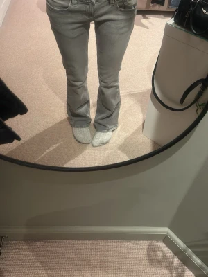 Grå bootcut jeans med fickor - Säljer ett par gråa bootcut jeans med klassiska fem fickor och låg midja. Jeansen har en snygg tvättad look och är tillverkade i ett mjukt denimtyg som sitter skönt. Perfekta för dig som gillar en avslappnad men trendig stil.