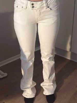 Vita jeans från 157 bootcut - Säljer ett par vita jeans från 157 med bootcut-modell och dubbla knappar i midjan. Jeansen har klassisk femficksdesign och är tillverkade i ett stretchigt denimtyg som sitter snyggt. Perfekta för dig som vill ha en clean och fräsch look.