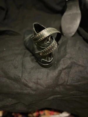 Svarta stövletter med nitar från Balenciaga  - Säljer ett par mörkgröna stövletter från Balenciaga i skinn  med två breda remmar runt ankeln, dekorerade med små guldfärgade nitar. Dragkedja baktill för enkel på- och avtagning. Snygg och edgy design som passar till många outfits.