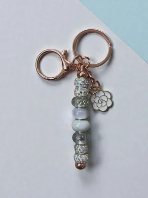 Nyckelring med pärlor och blomcharm - Snygg nyckelring med pärlor i silver, vitt och glitter samt en liten blomformad charm i metall. Nyckelringen har detaljer i roséguld och en mix av glittriga och transparenta pärlor som ger en trendig look. Perfekt att hänga på väskan eller nycklarna.