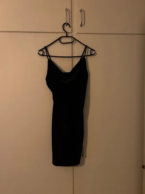 Svart kort klänning med smala band - Säljer en svart kort klänning med smala axelband och enkel, stilren design. Klänningen har en figurnära passform och är perfekt för dig som gillar minimalistisk stil. Materialet känns mjukt och följsamt mot kroppen.