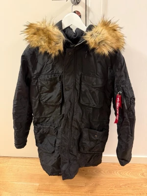 Svart parkajacka  - Snygg svart parkasjacka med stor huva och fuskpäls i brunt och beige. Jackan har flera praktiska fickor framtill och på ärmen samt dragkedja och knappar. Perfekt för kalla dagar och riktigt street-inspirerad look.