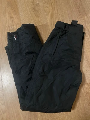 Skidbyxor/överdragsbyxor  - • Passar både vuxna och lite äldre/längre barn. Midjan har stretch, men kan också göras mindre med spännena (se bild) • Dragkedja finns längst ner vilket gör dom extra smidiga • Väldigt sparsamt använda