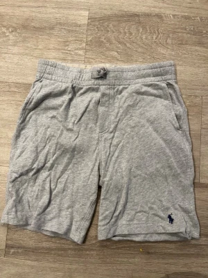 2-pack shorts från Polo Ralph Lauren - Två par mjuka shorts från Polo Ralph Lauren. Ena paret är ljusgrå med diskret logga i blått, det andra är ljusgula med större blå logga. Båda har snörning i midjan och sidofickor. Perfekta för chill dagar eller sommarhäng.