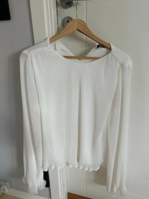 Vit blus med volangkant - Säljer en vit blus med långärmad design och rund halsringning. Blusen har fina volangdetaljer vid ärmslut och nederkant, vilket ger en extra touch. Materialet är lätt och stretchigt, perfekt för en trendig och stilren look. Använd en gång!!