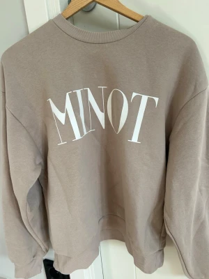 Beige sweatshirt MINOT Gina Tricot - Beige sweatshirt från Gina Tricot i storlek XS med trycket 'MINOT' i vitt på framsidan. Tröjan har rund halsringning, ribbade muddar vid ärmslut och nederkant samt en avslappnad passform. Tillverkad i mjukt sweatshirtmaterial, perfekt för en chill look.