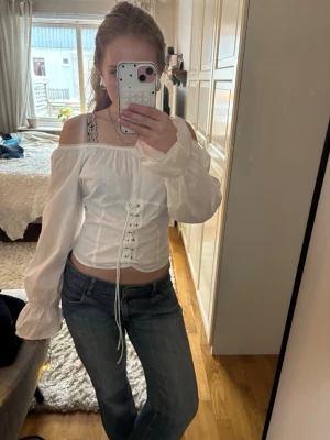Vit offshoulder korsettopp!! - Supercool topp med knytdetaljer/korsettdetaljer framtill! Smockad på baksidan och går att ha både vanligt och off shoulder😊 Köpt secondhand!! 100% Bomull! Säljer då den tyvärr är lite för stor för mig