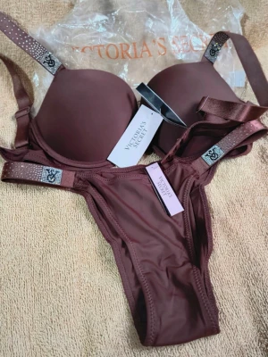 Brunt underklädesset Victoria's Secret - Snyggt brunt underklädesset från Victoria's Secret med vadderad bh och matchande trosa. Setet har glittriga detaljer på axelbanden och logotyp på banden. Materialet är mjukt och stretchigt för en bekväm känsla. 75C