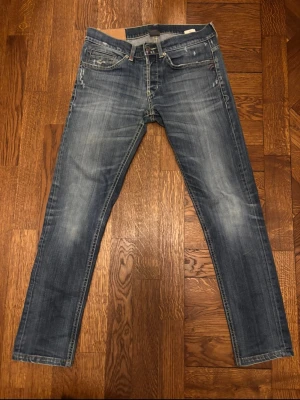 Dondup George  - Säljer ett par blå jeans från Dondup med snygga slitningar och tvättade detaljer. Modellen heter George. Klassisk femficksmodell med raka ben och normal midja. Jeansen har kontrastsömmar och en patch i läder bak i midjan. Perfekta för en avslappnad och trendig look.