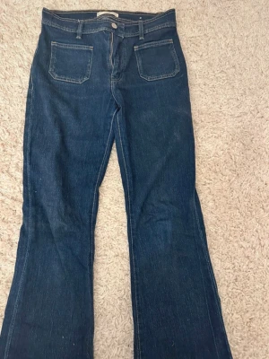 Mörkblå bootcut jeans - Säljer ett par mörkblå bootcut jeans med hög midja och raka ben. Jeansen har två framfickor och klassisk femficksdesign. Perfekta för dig som gillar en retroinspirerad look och vill ha ett par jeans som sticker ut lite extra.