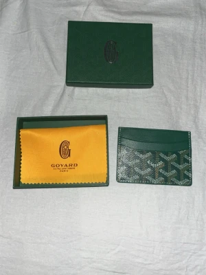 G-plånbok - Snygg och stilren i färgen grön med deras ikoniska mönster. Plånboken har flera kortfack och är tillverkad i skinn med tryckt logga framtill. Perfekt för dig som vill ha något exklusivt och smidigt i fickan.  