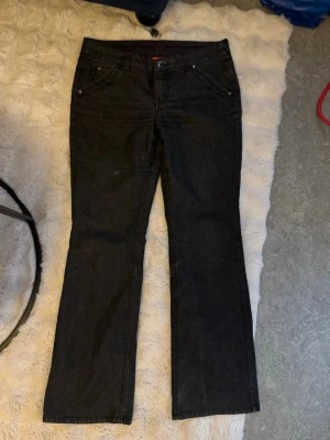 Svarta bootcut jeans med knappar bak - Snygga svarta jeans med bootcut passform och klassisk femficksdesign. Jeansen har två bakfickor baktill. 