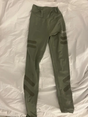 Olivgröna leggings från Aim'n - Snygga olivgröna leggings från Aim'n med hög midja och dekorativa mörkare ränder på benen. Tillverkade i stretchigt material som sitter skönt och följer kroppen.
