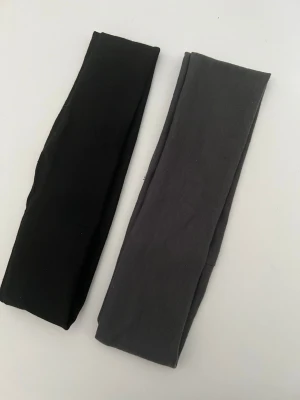 hårband - Säljer två hårband i svart och grått. De är tillverkade i mjukt och stretchigt tyg, perfekta för att hålla håret på plats. Passar både till träning och vardagslooken. Snygg minimalistisk design utan synliga loggor.